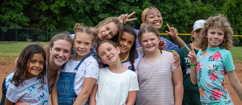 A group of girls and their counselors smile and make peace gestures with two fingers.