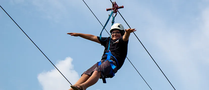 Camper smiles and stretches out hands on a zip line ride.