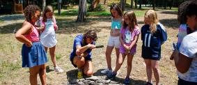 Campers observer a camp counselor demonstrating how to start a fire with a magnifying glass.